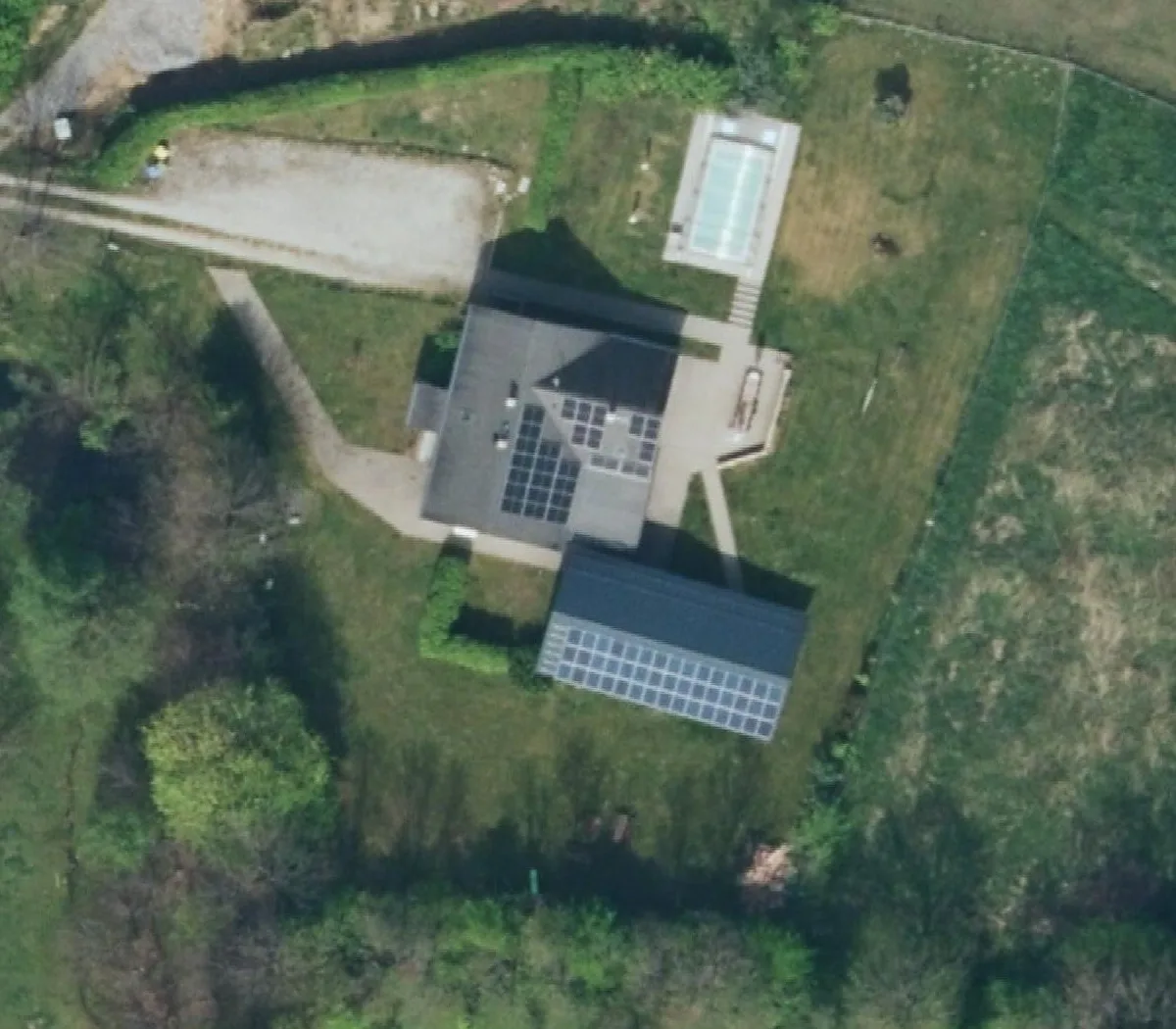 Letecký snímek pozemku chaty: dům se solárními panely, stodola, bazén, parkoviště, zahrada a louka